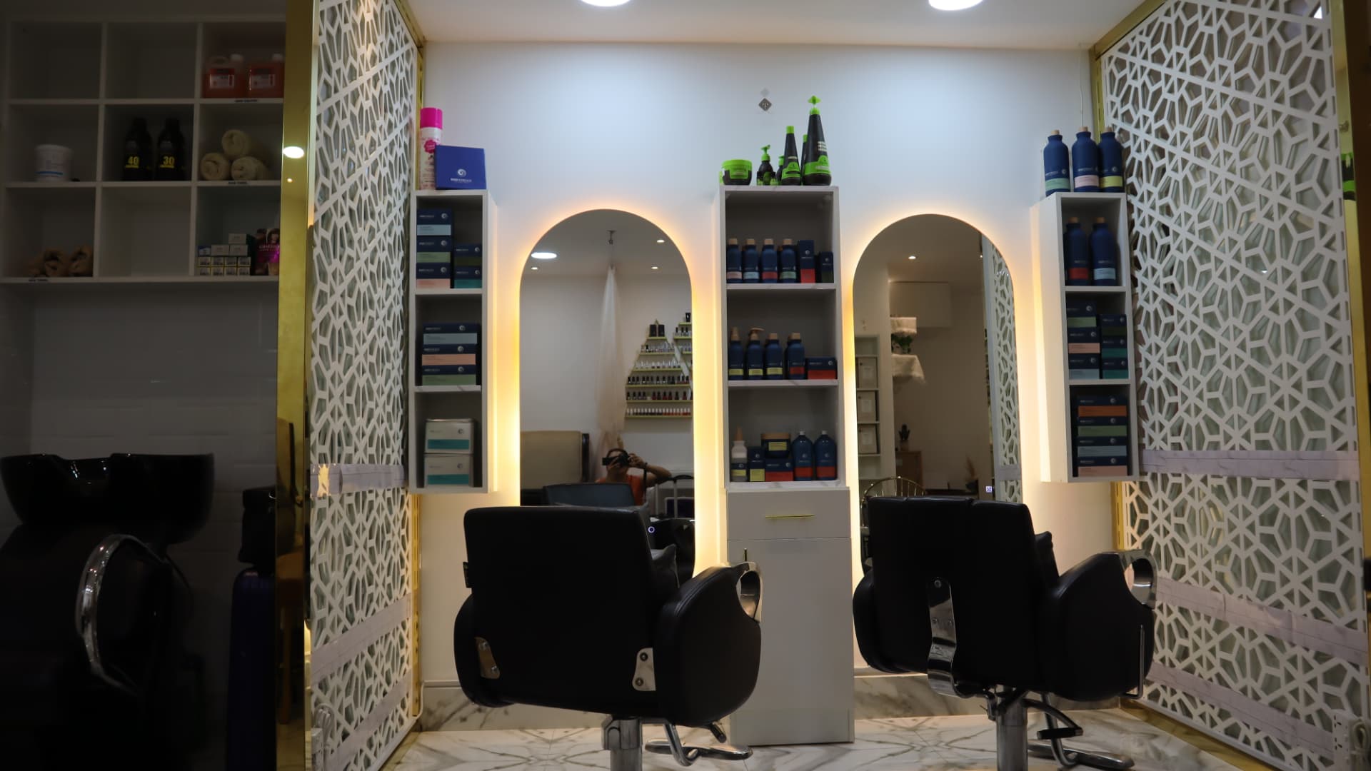 Salon stations with backlit arched mirrors, styling chairs and shelved hair products